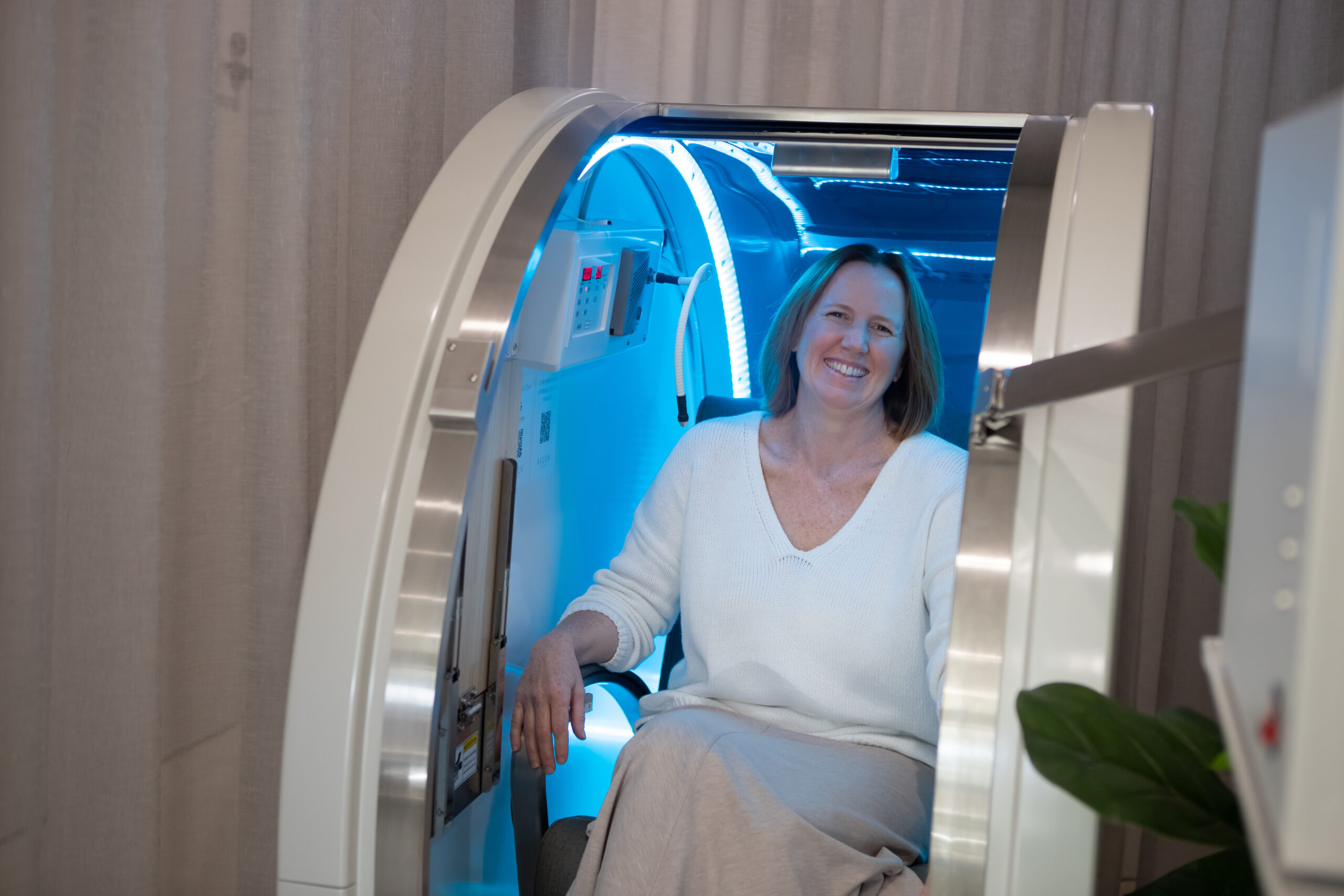 Caucasian Woman wearing white smiling while inside the Hyperbaric Oxygen Chamber at Hampton